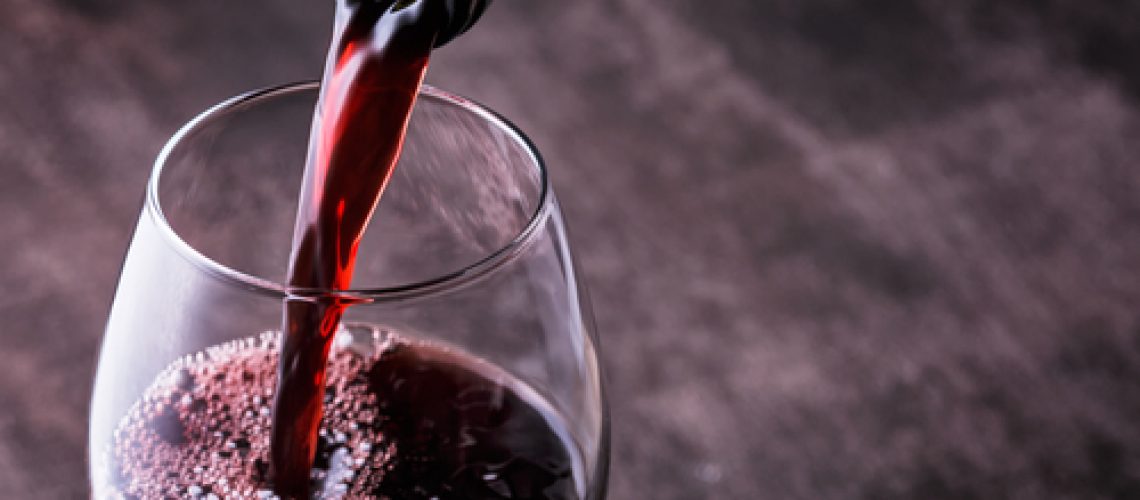 Pouring,Red,Wine,Into,The,Glass,Against,Wooden,Background